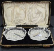 A cased pair of cut crystal butter dishes, of shaped oval form, each with silver butter knives,