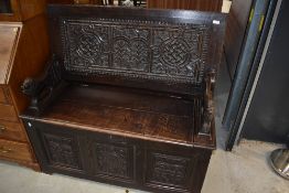 A traditional dark oak monks seat having heavily carved panels and lion arms