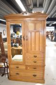 A Victorian wardrobe of aesthetic form with mirror door and stepped cupboard with drawer base