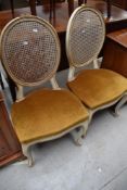 A pair of French style painted salon chairs having canework back and dralon upholstered seats