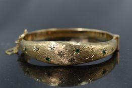 A 9ct gold hinged bangle having diamond and emerald chip decoration in star burst settings on