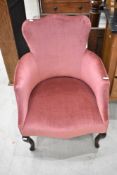 An early 20th Century low seat easy armchair and a similar mid 20th Century pink dralon footstool