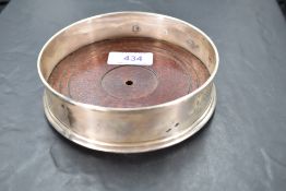 A modern silver wine bottle coaster having wooden base with plain silver collar bearing over sized