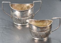 A late 19th/early 20th century sugar and cream, of half-fluted oval form with angular handles,