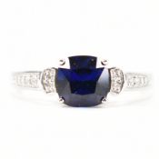 A hallmarked 9ct white gold synthetic sapphire and CZ ring. The ring set with a cushion cut