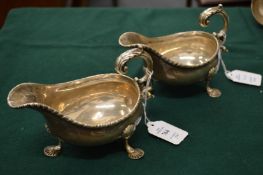 A pair of silver sauce boats with scrolling handles and shell cast feet.