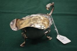 A silver sauceboat with scrolling handle and pad feet.