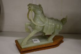 A Chinese carved jadeite model of a horse on a hardwood stand.