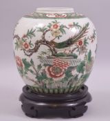 A GOOD CHINESE FAMILLE VERTE PORCELAIN JAR AND HARDWOOD STAND, painted with a peacock amongst native