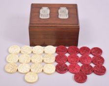 A SET OF FOURTEEN STAINED RED IVORY COUNTERS, and thirteen white counters, 4cm diameter, carved with