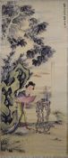 A CHINESE SCROLL PAINTING OF A FEMALE FIGURE, in a garden setting next to a root wood table with