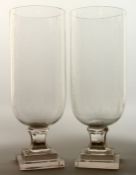 A GOOD PAIR OF GLASS STORM LAMPS on square stepped bases, 16ins high.