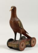 A PAINTED WOODEN FOLK ART BIRD, the base with four wheels. 8ins high.
