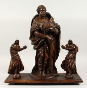 AN EARLY 17TH CENTURY CARVED WOOD SAINT holding a Bible and staff mounted on a wooden base with