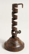 AN EARLY METAL CANDLESTICK on a circular wooden base. 8ins high.