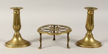 A CIRCULAR BRASS TRIVET, 5ins diameter and a pair of brass candlesticks, 6ins high. (3).
