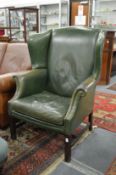 A Georgian style green leather upholstered wing armchair.