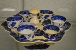 A blue and white Willow pattern egg cup cruet with six egg cups.