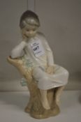 A Lladro figure of a boy seated on a tree stump.