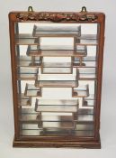 A SMALL CHINESE HARDWOOD WALL CABINET, with glazed door encasing five shaped shelves in front of a