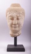 A LARGE EARLY CHINESE STONE HEAD OF BUDDHA, mounted on a wooden stand, the head 46.5cm high.