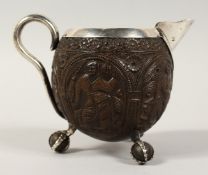 A SILVER CARVED COCONUT SKULL JUG with carved panels on claw and ball feet. 3.5ins diameter.