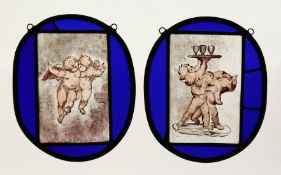 A PAIR OF OVAL BLUE GLASS LEADED LIGHTS decorated with cupids. 9.5ins x 8ins.