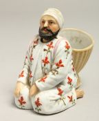 A SMALL ARAB PORCELAIN FIGURE of a man carrying a basket, with a nodding head. 3.5ins high.