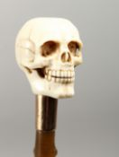 A RUSTIC RHINO PART RIDING CROP with carved ivory skull handle. 10ins long.