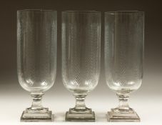 A SET OF THREE CUT GLASS STORM LAMPS on a square stepped bases. 15ins high.