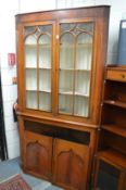A 19th century fruitwood standing corner cabinet with a pair of glazed doors over a pair of panel