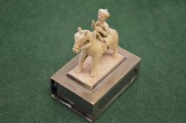 A carved figure on horseback mounted on a silver matchbox case.