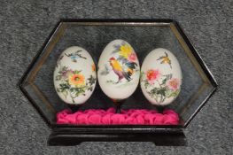 Three Chinese painted eggs in a glass case.