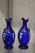 A pair of painted blue glass ewers.