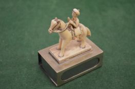 A carved figure on horseback mounted on a silver matchbox case.