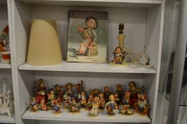A large collection of Hummel figures, a table lamp and book.