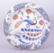 A TURKISH OTTOMAN IZNIK POTTERY DISH, the centre painted with a peacock and flora, 31cm diameter.