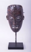 A SMALL CARVED WOOD AFRICAN MASK, raised on a wooden stand, mask 18cm x 11.5cm.