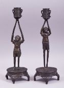 A PAIR OF JAPANESE BRONZE FIGURAL CANDLESTICKS, each formed as a male figure upon a base with arms