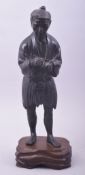 A JAPANESE MEIJI PERIOD BRONZE OKIMONO of a man holding a pipe, mounted to a carved hardwood base,