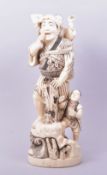 A LARGE CARVED IVORY FIGURE OF A MAN WITH CHILDREN, the figure stood upon a rocky base with waves, a