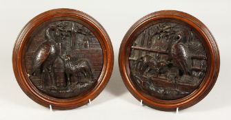 A PAIR OF BLACK FOREST CARVED WOOD CIRCULAR PLAQUES, depicting Aesop's fable of the Fox and Stork.