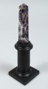 AN AMETHYST OBELISK on a wooden stand 4ins high.
