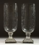 A PAIR OF GLASS STORM LAMPS on stepped square bases. 16ins high.