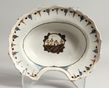 A CONTINENTAL TIN GLAZE SHAVING DISH, the centre painted with a cottage and flowers. 13ins long.