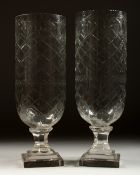 A PAIR OF GLASS STORM LAMPS on stepped square bases. 13ins high.