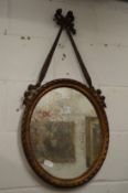 A decorative oval mirror with ribbon cresting.