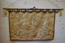 A Chinese embroidered silk picture on an ornate brass hanging pole.