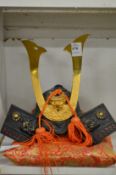 A cast metal model of a Samurai helmet on a gilt embroidered cushion.