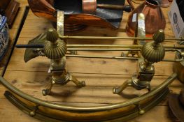 A pair of brass fire dogs, three fireside tools and a fender.